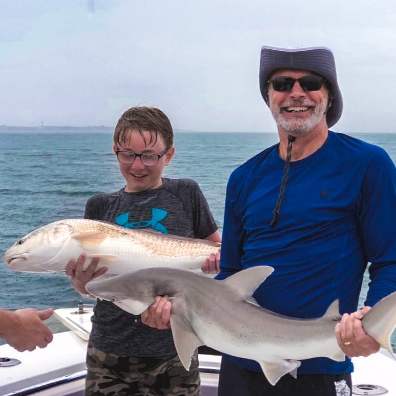 Father and son during a fishing trip, with a bull red and shark