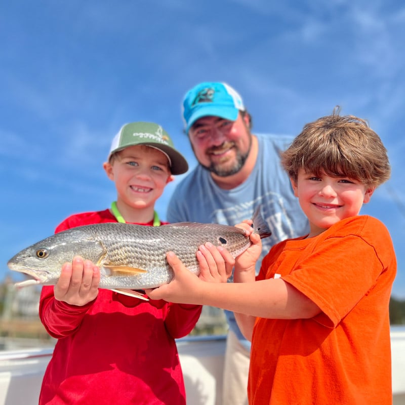 Father and two young sons holding spot tail fish